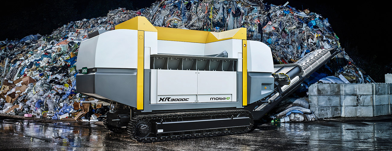 Stor, långsamtgående enstegskross framför en stor avfallshög